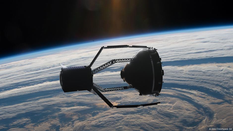 A spider-like space vehicle extends four arms towards a floating piece of space junk above Earth