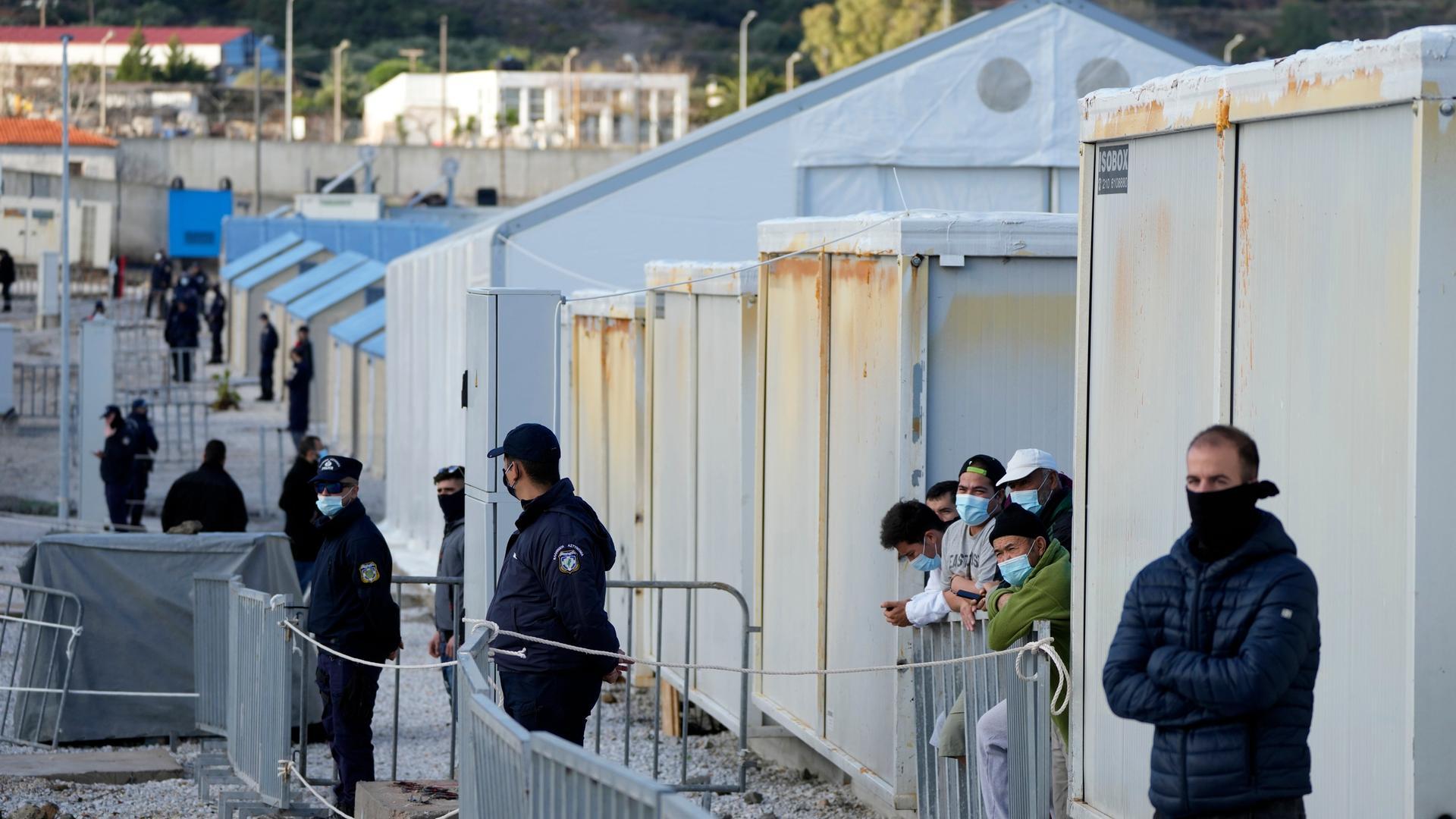 Flüchtlingslager auf der griechischen Insel Lesbos am 5. Dezember 2021. Blick an einer Container-Hausfront entlang, mehrere Flüchtlinge stehen wartend am Rand.