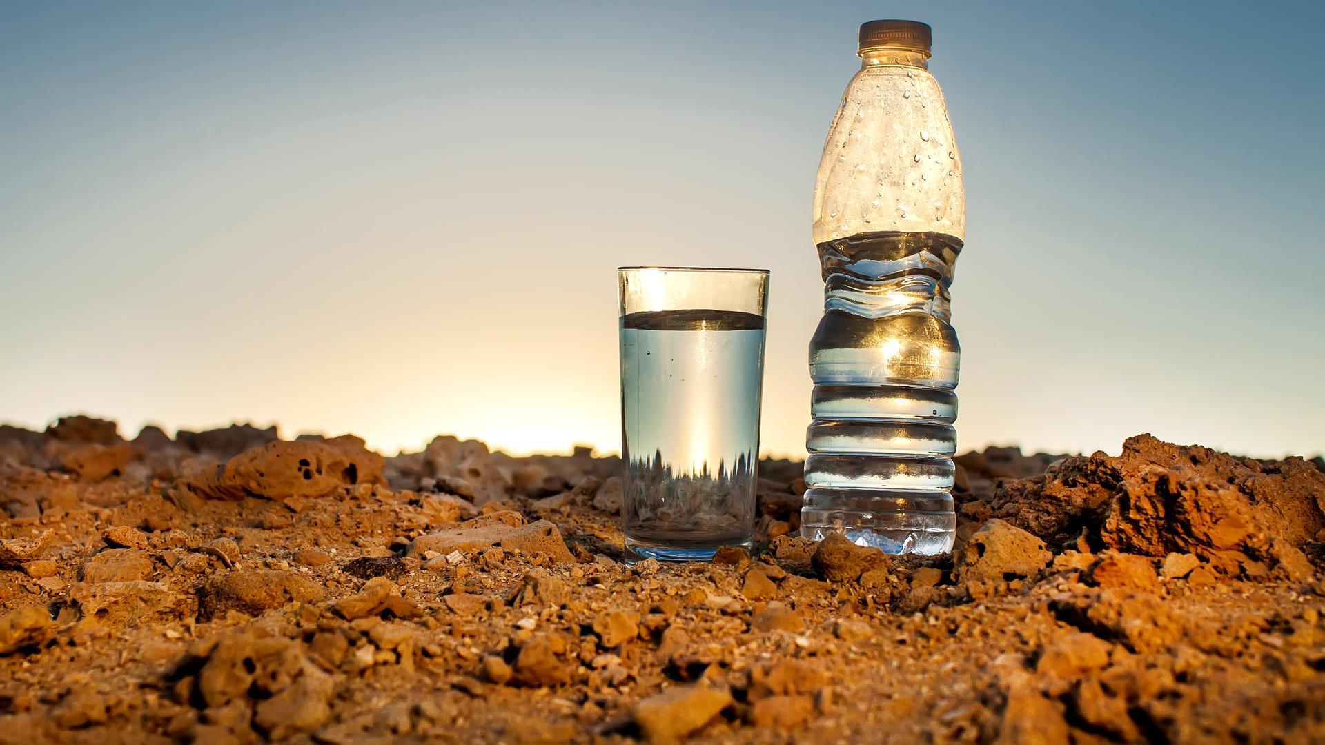 Eine Flasche Wasser und ein Glas stehen in einer Steinwüste. 