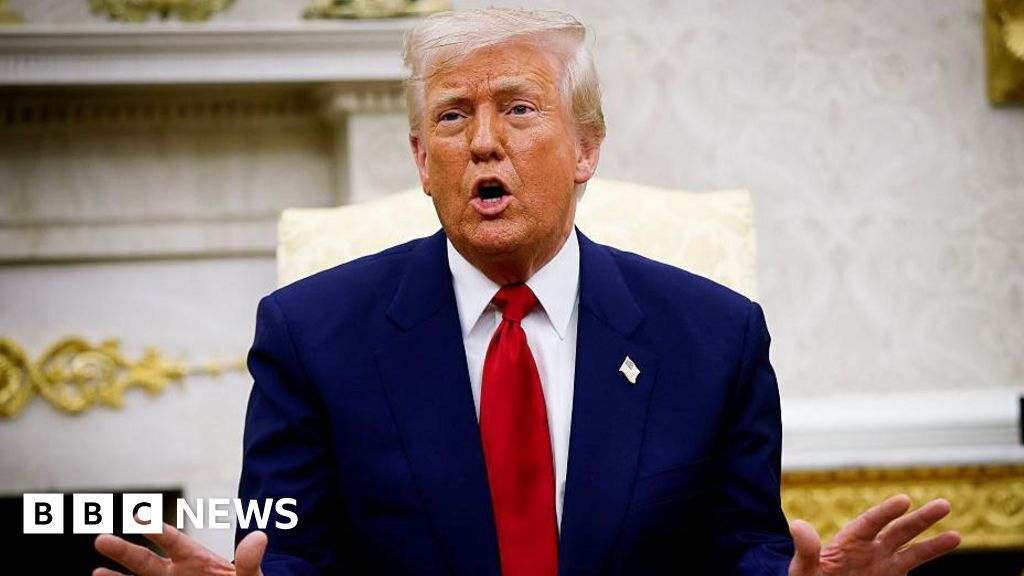 US President Donald Trump speaks during a meeting in the Oval Office. The president has his hands out and is talking. His wearing a blue suit and a red tie.