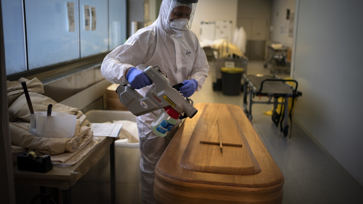 A mortuary worker disinfests a coffin carrying the body of a person who died of COVID-19 ahead of a funeral at Memora mortuary in Girona, Spain, Thursday, Feb. 4, 2021. (AP Photo/Emilio Morenatti, File)