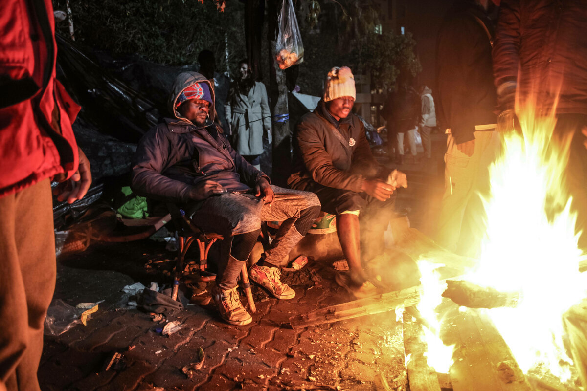 Eine Gruppe ärmlich gekleidter schwarzen Migrant sitzt am Feuer, einer ruht erschöpft