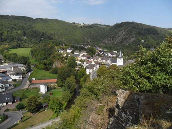Blick von einem Felsen auf einen Ort namens Schuld (an der Ahr) mit einer Kirche, dahinter steile Felsen