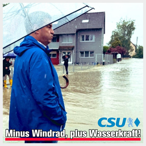 Pressefoto: Markus Söder (CSU) steht in blauer Regenjacke mit durchsichtigem Regenschirm in einer stark vom Hochwasser betoffenen Ortschaft. Dazu der Text »CSU: Minus Windrad, plus Wasserkraft«. 