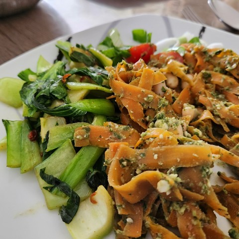 Pesto-Karottennudeln mit weißen Bohnen und Tomaten und Pak Choi Gemüse auf weißen Teller angerichtet.  Großaufnahme.