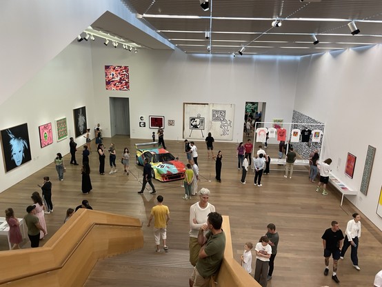 A modern art gallery with visitors viewing various artworks and a colorful car display.