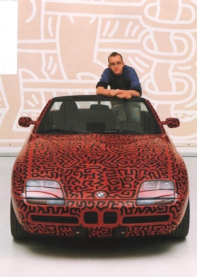 Person leaning on a BMW car with intricate red and black patterns, standing in front of a matching abstract mural.