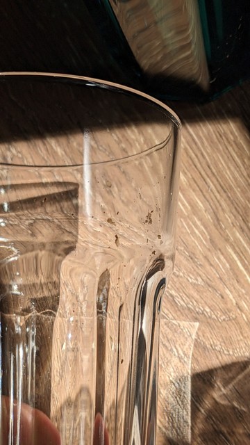 Nahaufnahme eines Glases mit Dreckablagerungen in der Mitte. Im Hintergrund ist eine braune Küchenplatte zu erkennen.