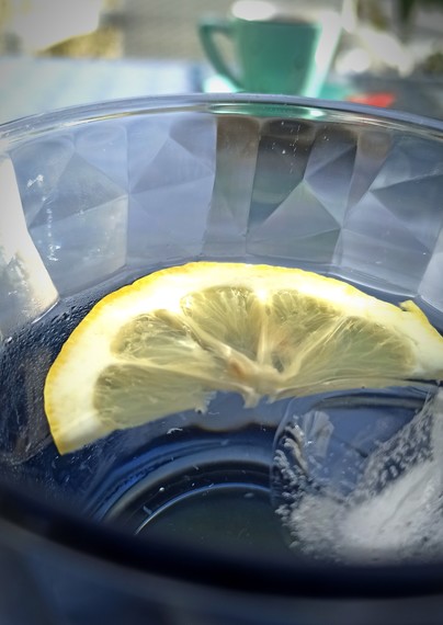 halbe Zitronenscheibe in blauem Wasserglas