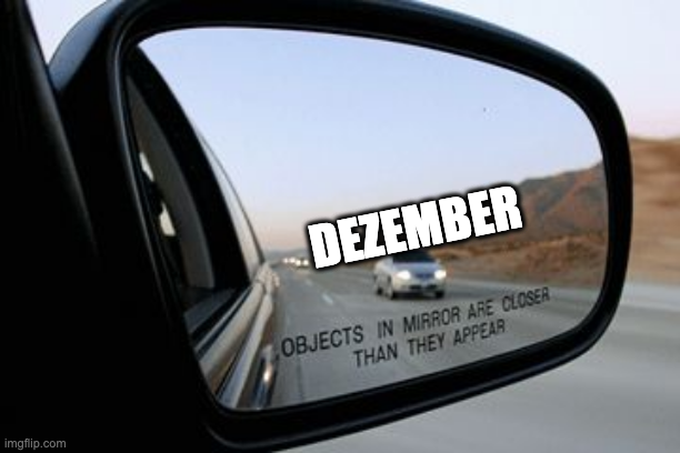 Spiegelbild aus einem rechten Aussenspiegel. Es ist die Aufschrift "Objects in Mirror are closer than they appear" zu sehen, der auf dem Spiegel aufgedruckt ist. Es nähert sich ein Auto, das mit "Dezember" betitelt ist.