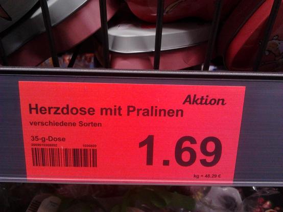 Preisschild in einem Supermarkt: »Aktion – Herzdose mit Pralinen – verschiedene Sorten – 35-g-Dose – 1,69 €«.