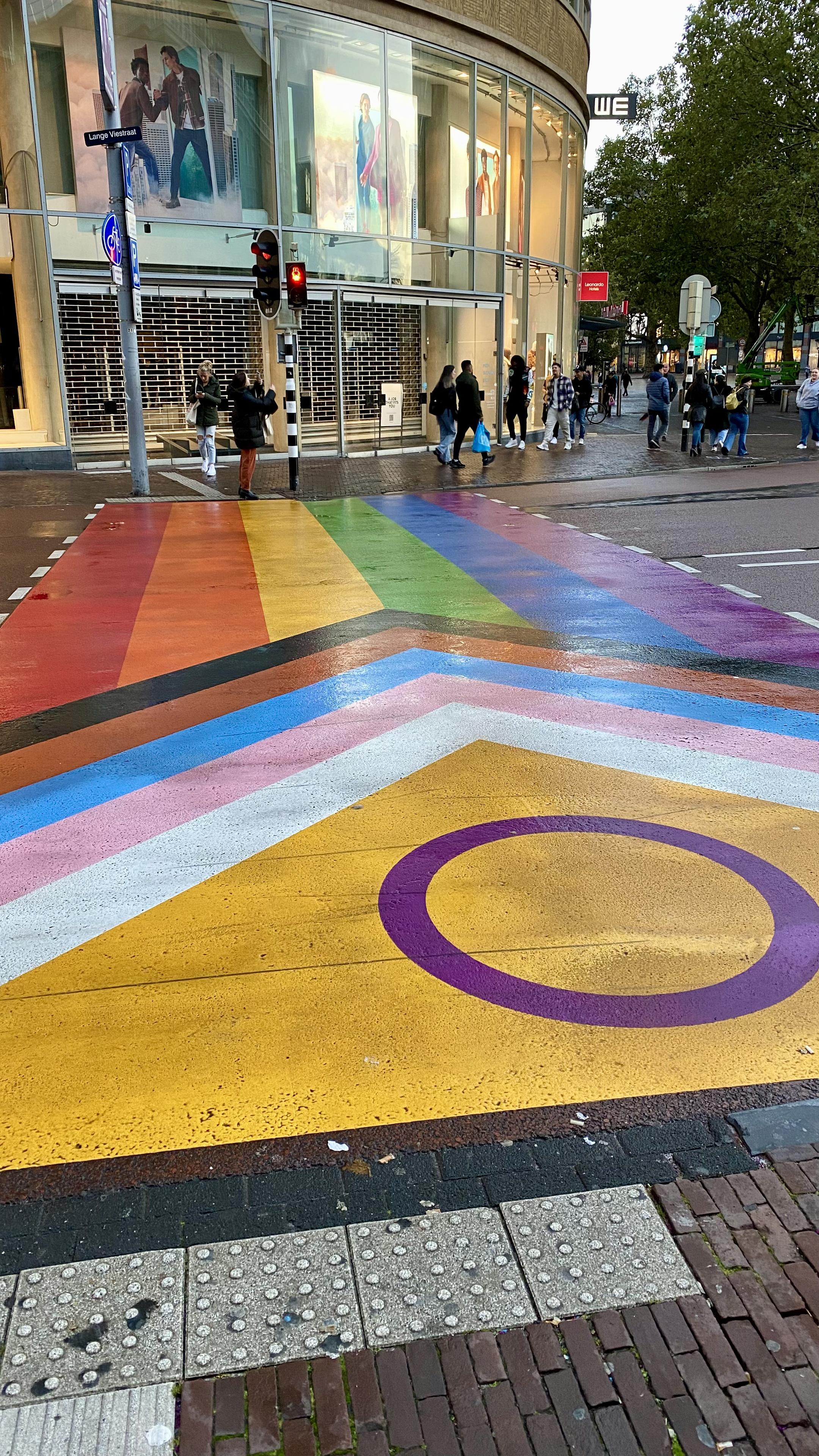 Ein Regenbogen ist anstelle eines Zebrastreifens auf die Straße gemalt. Der Regenbogen bildet die LGBTQ Flagge ab.