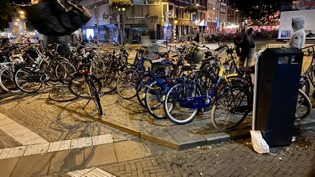 Eine Menge Fahrräder, die dicht gedrängt auf einer Art kleinen Verkehrsinsel geparkt sind. Das Foto ist nachts entstanden, das Laternenlicht färbt die Szene in gelbliches Licht.