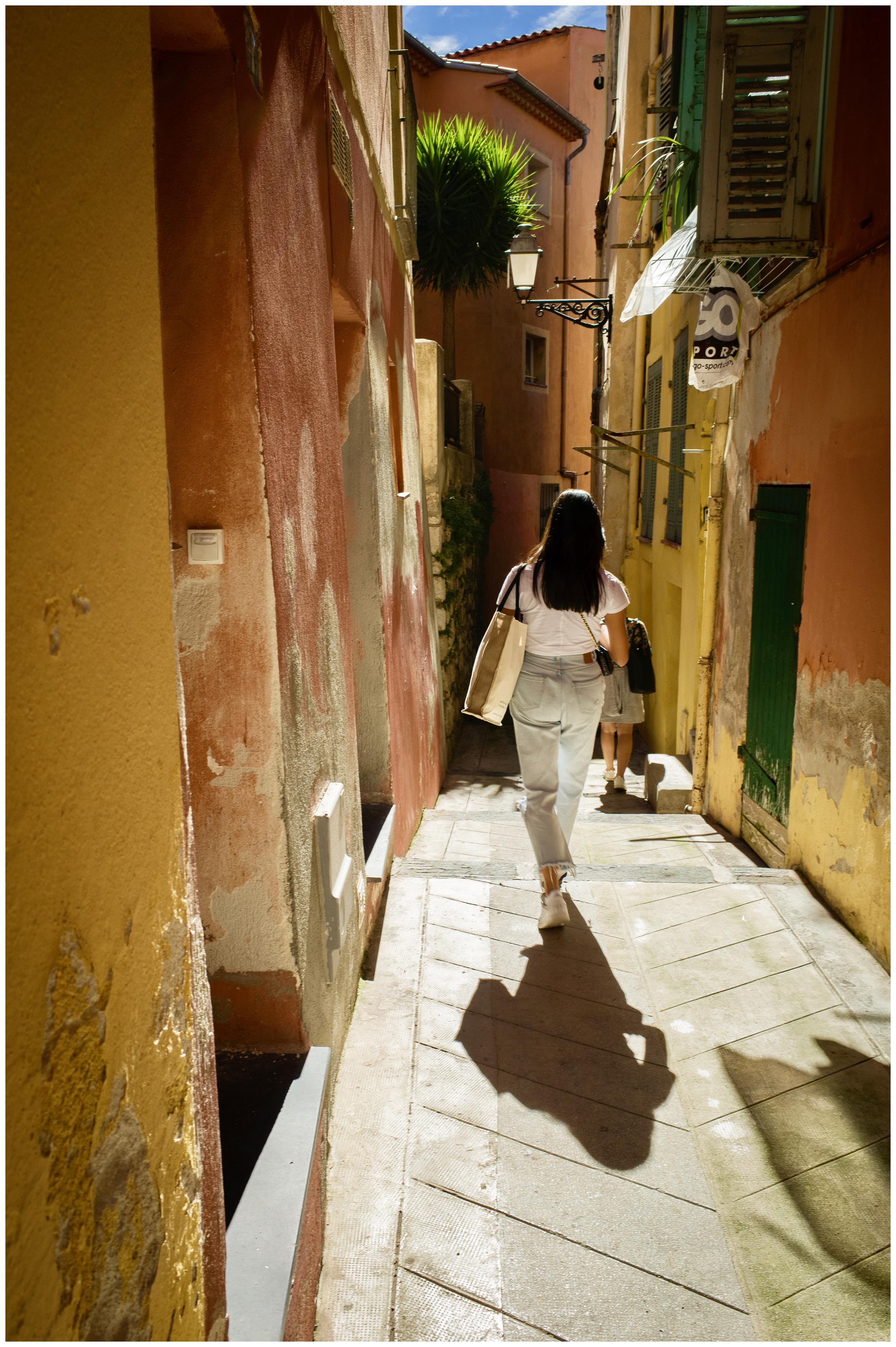Junge Frau von hinten, die eine kleine Gasse in der Altstadt von Nizza hinuntergehet.