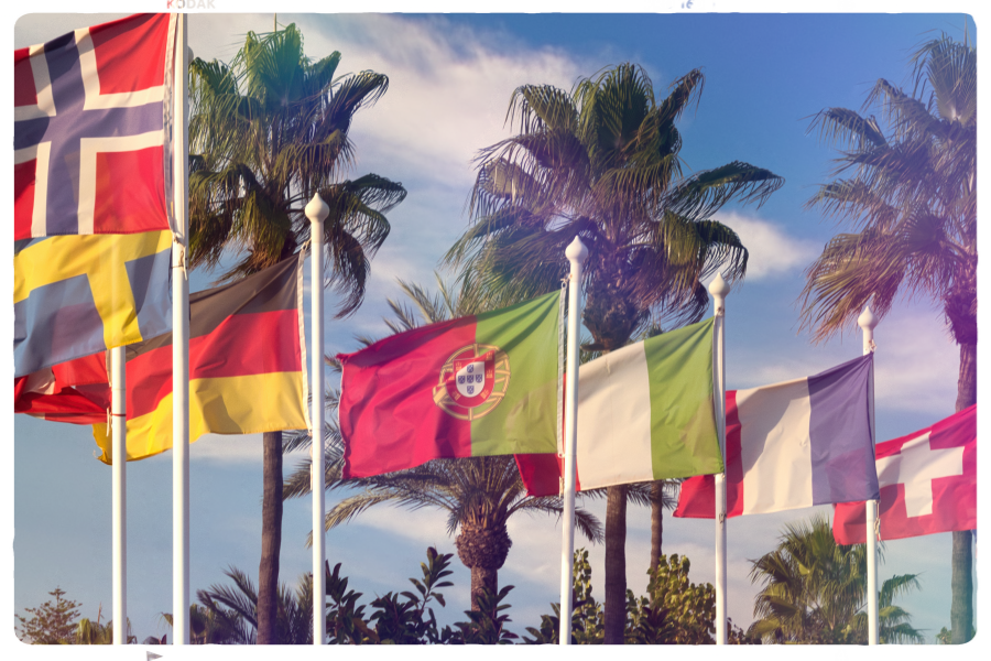 Auf einem etwas verblichenen Urlaubsfoto flattern sieben sichtbare Nationalflaggen Europas: von links nach rechts Norwegen, Schweden, Deustchland 
-mittig- Portugal, Italien Frankreich und der Schweiz. Ganz rechts wäre noch Großbritannien gewesen, hat nicht mehr auf das Bild gepasst. Dahinter Palmen und blauer Himmel.